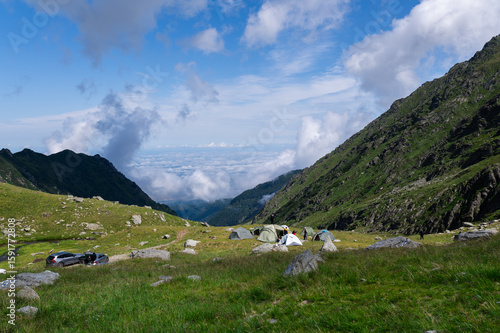 Mountain camping site with tents and parked cars in a grassy alpine valley above the Transfagarasan road in the Fagaras Mountains, Romania. Cloudy summer day in the Southern Carpathians.