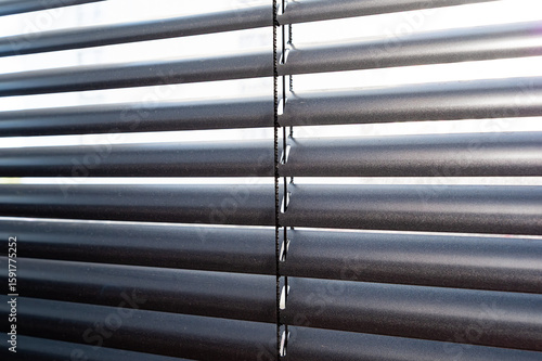 Close-up of horizontal aluminum blinds in sunlight. Detail of slats and cords creating repetitive pattern and modern texture