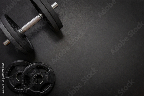 Black dumbbell and weights lying on a dark gym floor, creating a fitness-focused composition with ample copy space