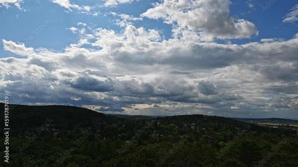 Time lapse of a dramatic sky filled with thick clouds stretches above a landscape of lush green hills and scattered homes. The sunlight filters faintly through the clouds. Time lapse of a dramatic sky filled with thick clouds stretches above a landscape of lush green hills and scattered homes. The sunlight filters faintly through the clouds.