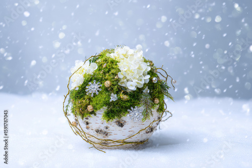 A delicate floral arrangement features white flowers and vibrant moss, artfully crafted and set against a backdrop of softly falling snowflakes in winter