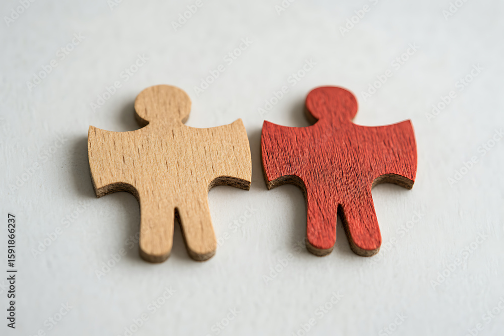Fototapeta premium Two wooden figures, one natural and one red, symbolize diversity and connection, highlighting individuality within unity.