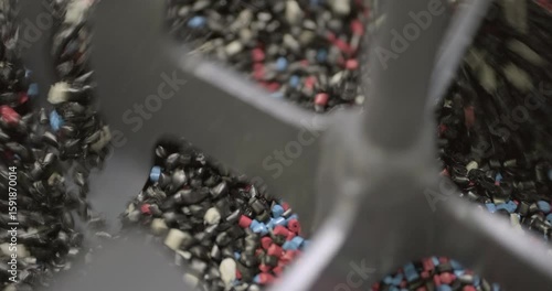Pieces of multi-colored plastic are mixed in an industrial mixer before being disposed or reused. Close up handheld shot, real time speed, artificial indoors lighting.