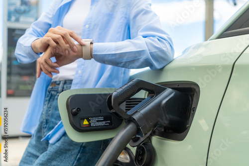 Close up of electric car driver looking at time on watch while waiting to charge electric car for next safe drive. Future energy concept