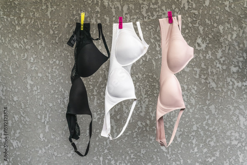 Konstfotografi Three washed bras hang on a clothesline against a gray wall.