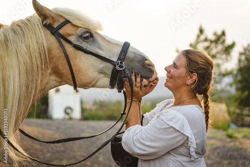 woman in her 40s taking care of her horse in the barn, smiling and bonding at sunset