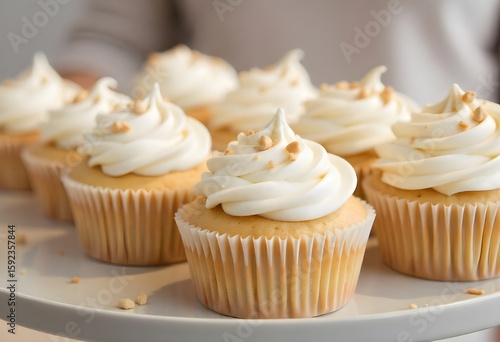 Freshly baked vanilla cupcakes topped with smooth white frosting and a sprinkle of nuts, arranged neatly on a white tray