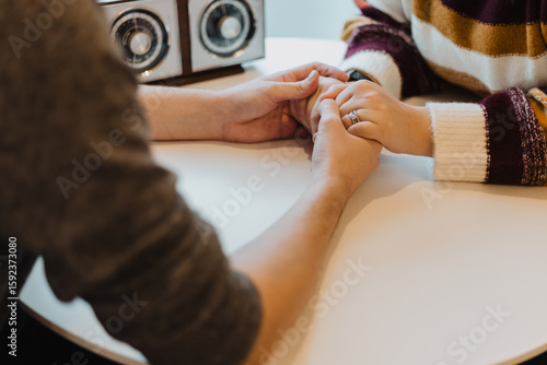 Tablou pe pânză Close-up of couple holding hands across a round table, symbolizing emotional sup