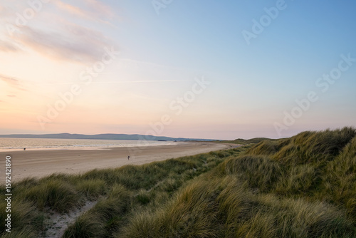 Sandy beach and grassy dunes at sunset.