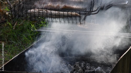 Grilled fish in barbecue grill grid turning over. Roasted mackerel fish fillets on charcoal grill in smoke. Cooking on bbq grill