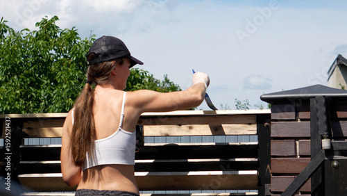 Painting a fence. Gardening, woman paints a fence with black paint with a brush. Fence renovation, woman painter paints a fence