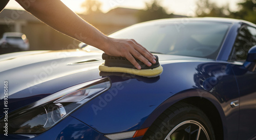 Man polishing a blue sports car with wax during sunset