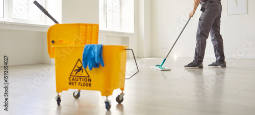 Photos Janitor with mop cleaning empty office floor, worker mopping by yellow cart with professional cleaners supplies and warning wet floor sign to clean room