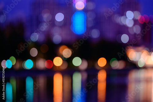 Colorful city lights bokeh at night with reflections on water, abstract defocused urban background with vibrant glowing circles, dreamy atmosphere and evening cityscape light blur