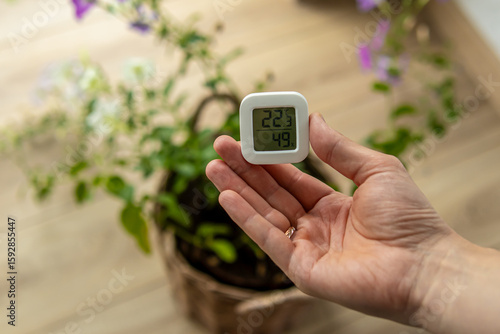 Man holds small digital indoor temperature and humidity meter. Temperature sensor. Growing flowers at home