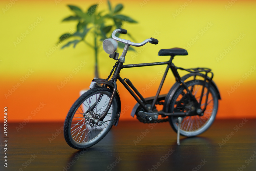 Fototapeta premium Vintage bicycle miniature against a gradient background with a decorative plant providing a warm nostalgia