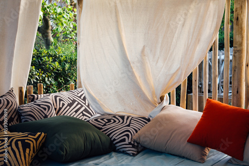 Coussins et oreillers sous un voilage de pergola. Lieu de repos et de relaxation. Rideaux blanc et oreillers confortables pour une ambiance zen. Pergola en été.