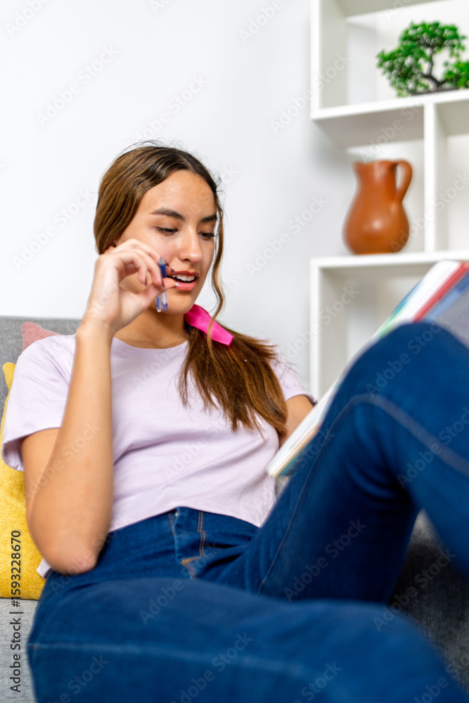 Young student doing homework and holding pen in living room Young student doing homework and holding pen in living room