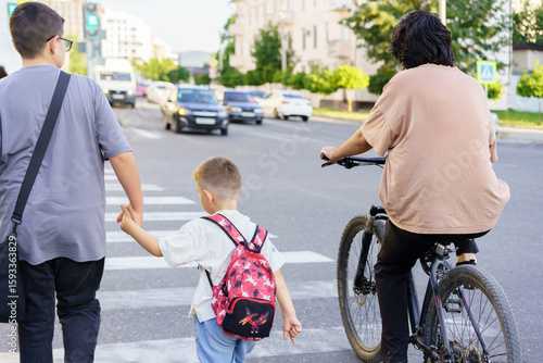Family crossing the street together on a sunny day while a cyclist passes by in a suburban area