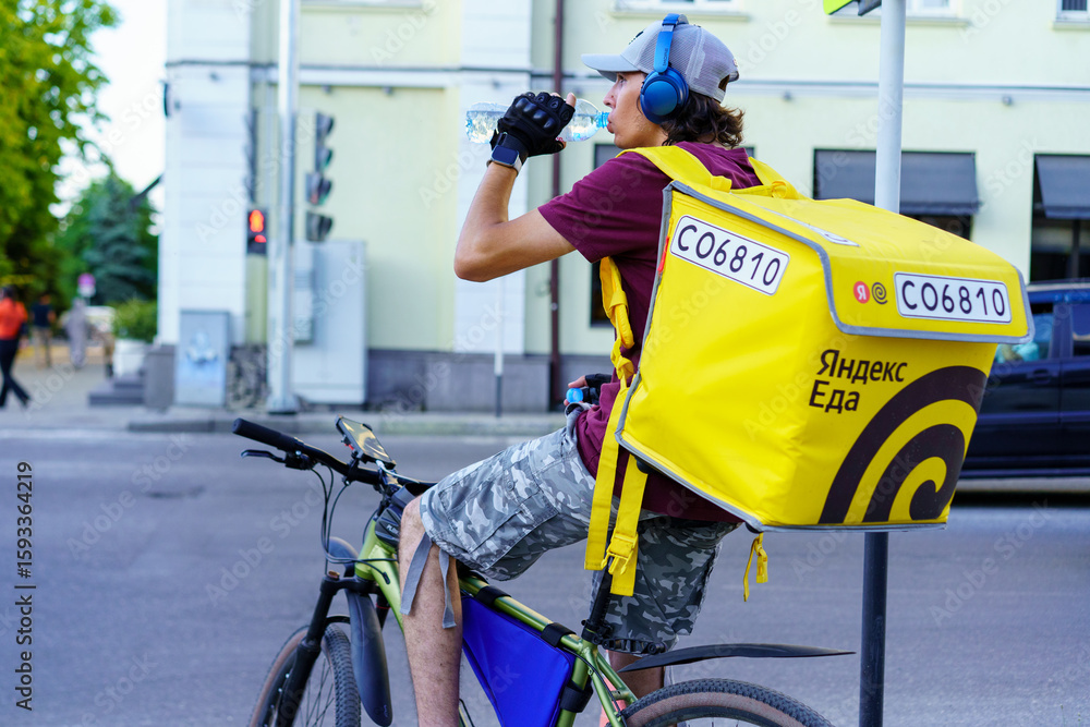 Fototapeta premium Delivery cyclist takes a break to hydrate in the city on a warm afternoon while waiting for the next order