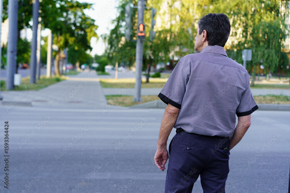 Obraz premium Man waiting at a crosswalk in a quiet urban area during the daytime