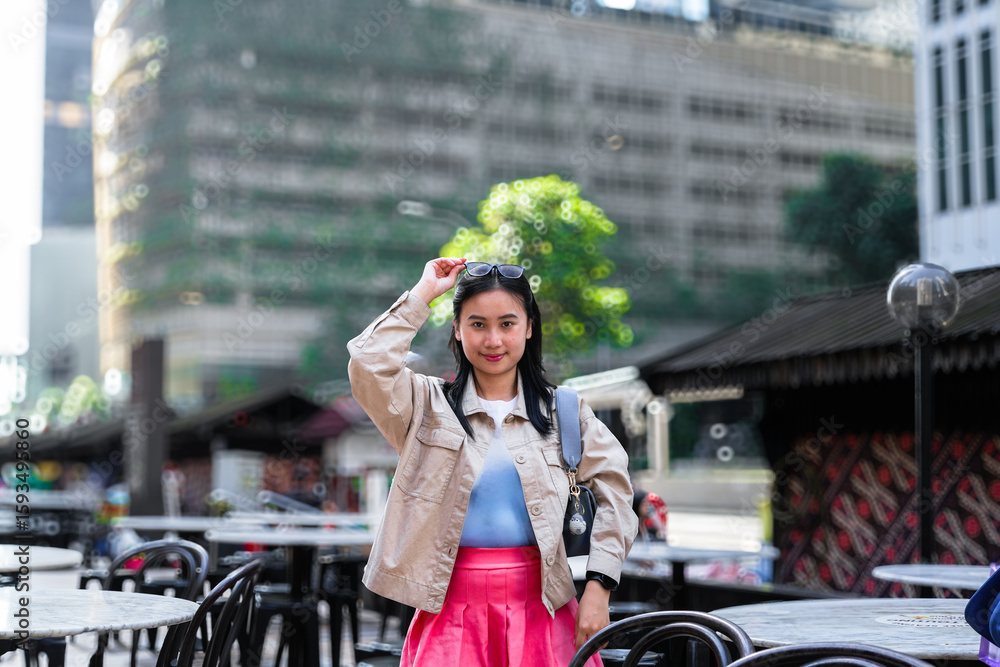 Fototapeta premium The image shows a young woman posing for a photo outdoors in an urban setting. She is wearing a light-colored jacket