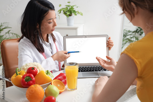 Female Asian nutritionist working with laptop and patient in office
