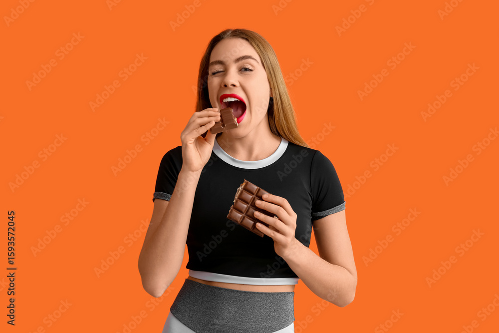 Young woman eating chocolate bar on orange background Young woman eating chocolate bar on orange background
