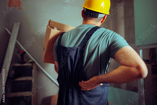 Construction Worker Complaining of Back Pain Lifting Heavy Box. Man doing physical labor getting injured at the workplace 
