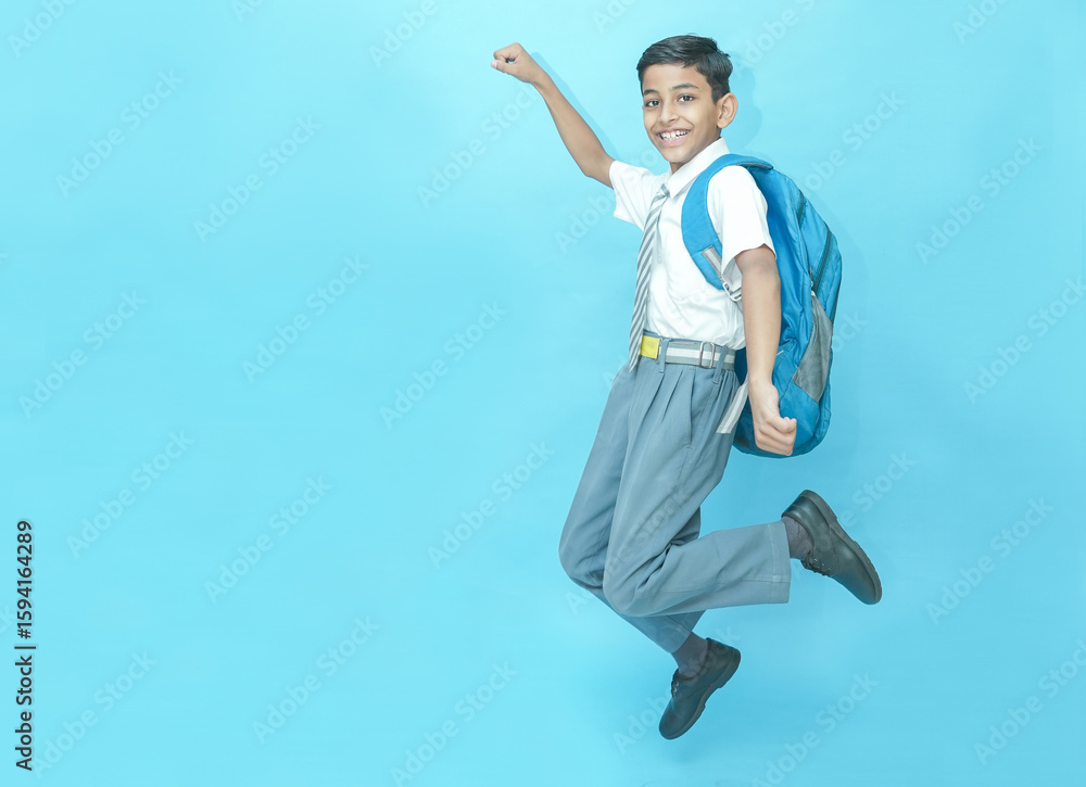 Fototapeta premium Excited Indian schoolboy student jumping with joy isolated over blue background, Education knowledge concept. Admission open.