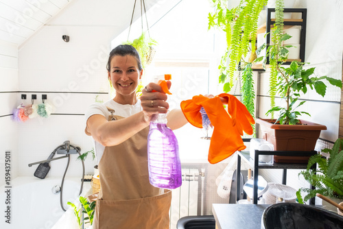 Photos Portrait Woman in rubber gloves and apron manually cleaning in bathroom with rag cleaner and mop inside interior with home plants