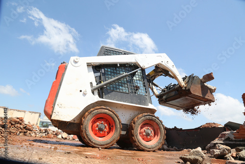 skid steer loader working construction site. mini loader transports excavation waste at construction site. compact loader. skeed steer workingi on site. compact construction machinery.