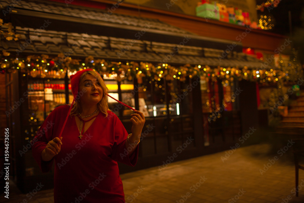 Obraz premium Plus size woman walks around the city during the Christmas of the week with a hot drink in a glass against the background of flickering light bulbs