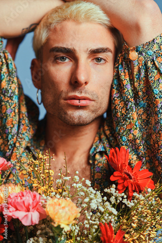 Young male model with bouquet of fresh flowers with raised arms and looking at camera against blue background