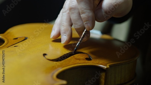 Skilled luthier brushing dark varnish on handcrafted violin, applying traditional antiquing method to emphasize musical instrument's vintage aesthetic