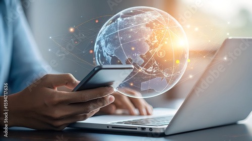 Person using smartphone and laptop with holographic globe overlay