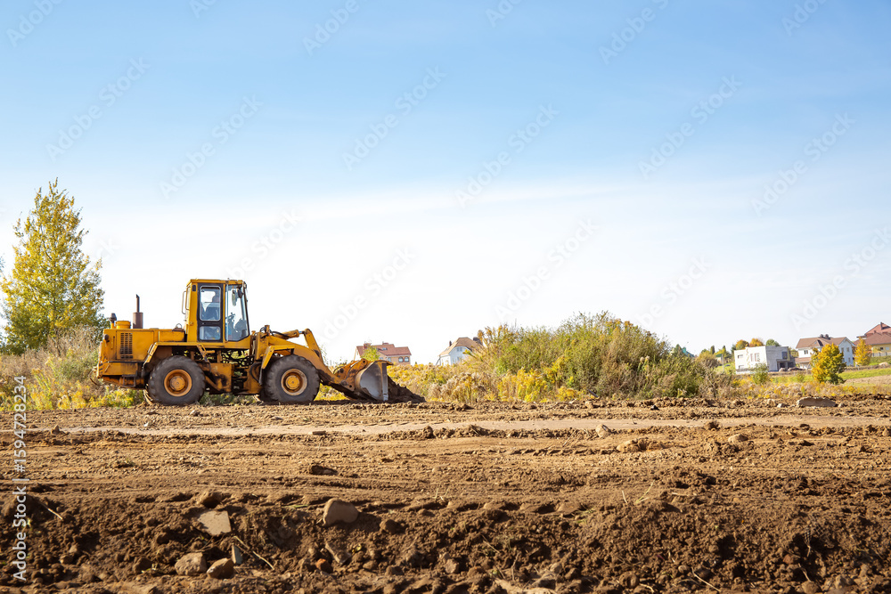 Obraz premium Yellow bulldozer at a construction site. Big wheel excavator leveling and clearing the land plot side view. Moving earthworks soil. Copy space. Building area. Special transport. High quality photo.