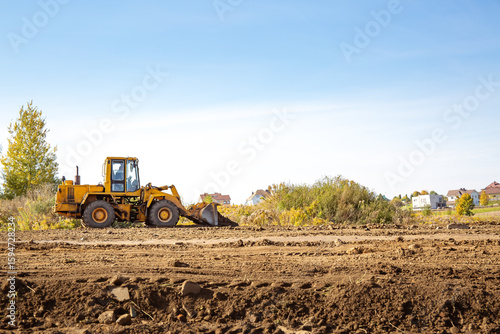Yellow bulldozer at a construction site. Big wheel excavator leveling and clearing the land plot side view. Moving earthworks soil. Copy space. Building area. Special transport. High quality photo.