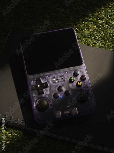 A transparent portable retro gaming console with a large screen and several buttons, including directional controls, analog sticks, and buttons labeled X, Y, A, and B.