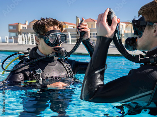 Close-up of two scuba divers in a pool at a dive resort practicing skills, holding their inflator hoses up and their regulators in their mouths. Getting ready to submerge.