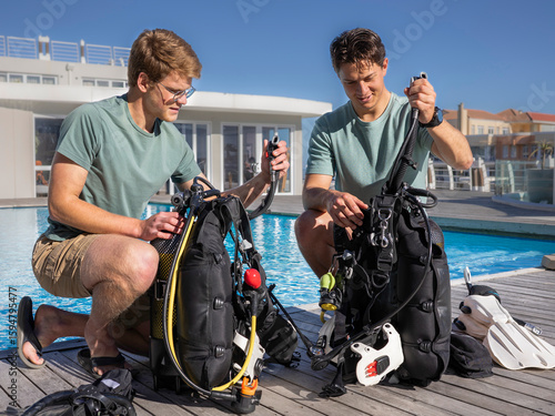 Two scuba divers wearing summer clothes are getting their gear ready next to a pool at a dive resort. Checking gear by inflating BCDs.