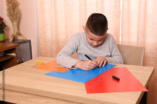 Bild auf Leinwand A boy makes applications from colored paper while sitting at a table