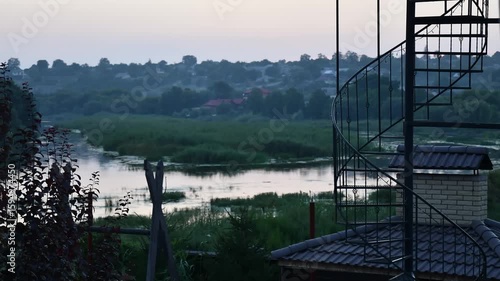 Time lapse showcasing persons ascending winding staircase against backdrop of lush greenery and tranquil waterway at dusk. Serene moment of nature and adventure over river Southern Bug in Ukraine