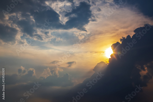 Dramatic cloudy sky with golden sunlight breaking through at sunset. A mix of dark storm clouds and soft illuminated areas creates a moody and atmospheric scene.