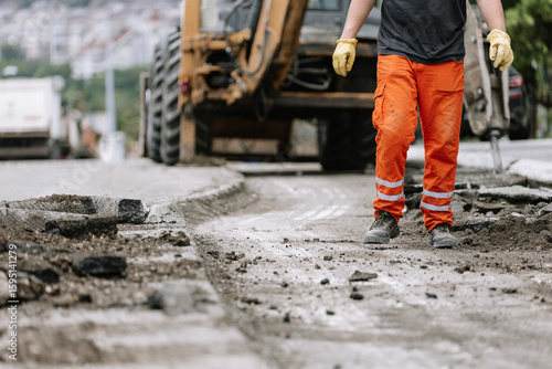 Construction worker repairs the street in urban area during daylight hours with heavy machinery nearby