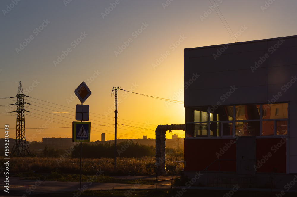 Obraz premium A road sign and other infrastructure in the light of the setting sun