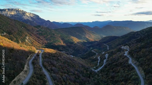  Winding mountain road in Vercors seen from Col de Rousset at sunset, cars driving through forested slopes in Drome region, southeastern France
