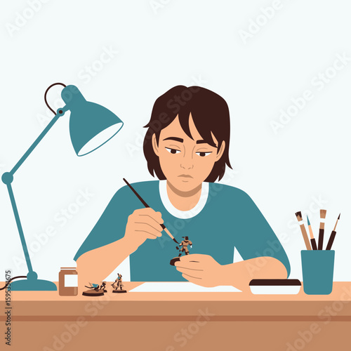 Focused young person meticulously paints miniature figures at a desk, illuminated by a desk lamp.