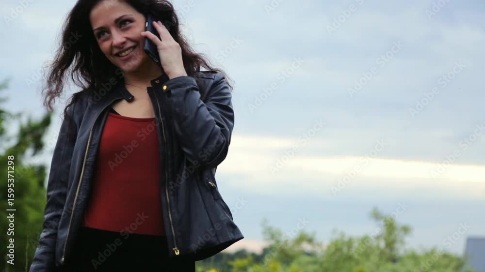 Happy smiling face of woman talking on mobile phone in business clothes enjoying nature with blue sky and green trees during summer sunset outdoors Happy smiling face of woman talking on mobile phone in business clothes enjoying nature with blue sky and green trees during summer sunset outdoors