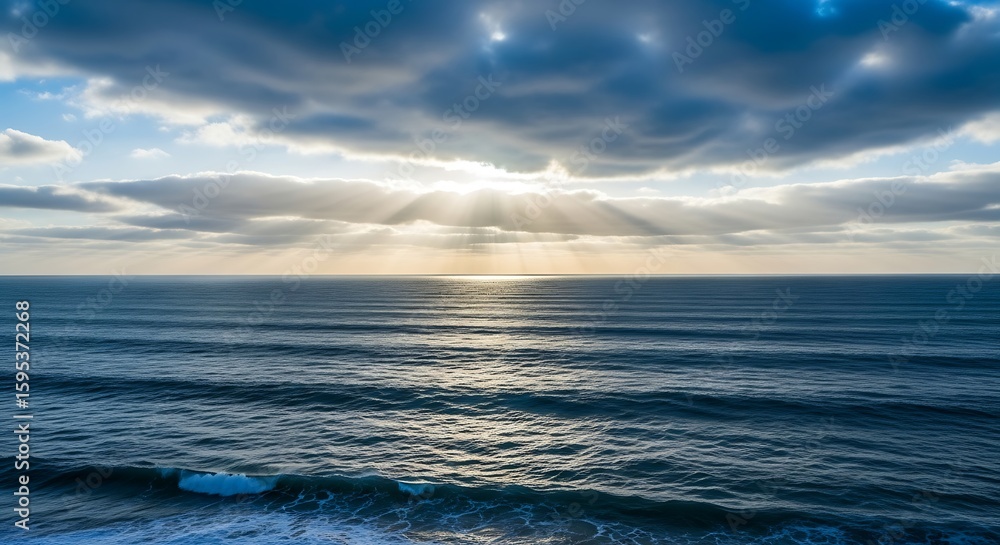 Obraz premium Majestic seascape featuring sunlight beaming through clouds over rippling ocean waters